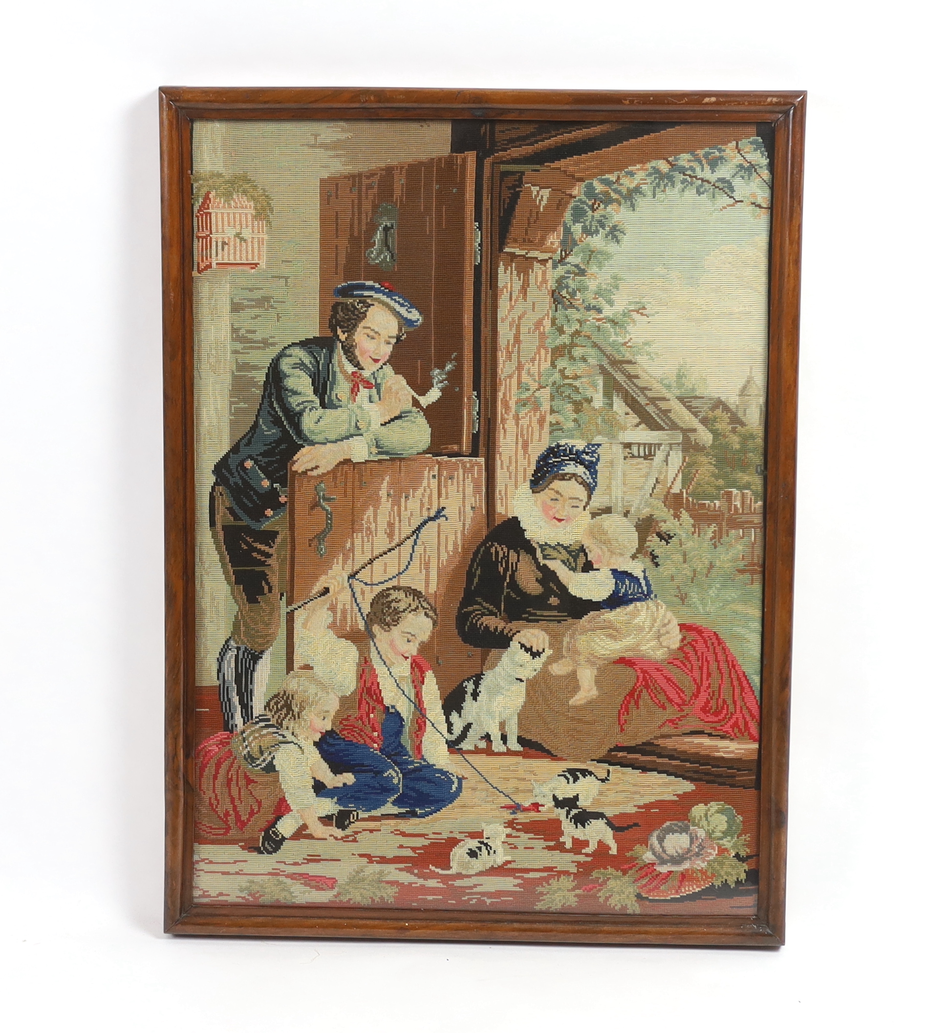 A framed 19th century Berlin woodwork embroidery of a Scottish farmhouse scene, embroidered with children and kittens playing, a mother, baby and father smoking a clay pipe, wearing a Tam o'Shanter leaning on a door, 53c